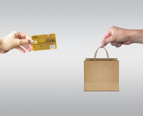 Zwei Hände tauschen eine Kreditkarte für eine Einkaufstüte