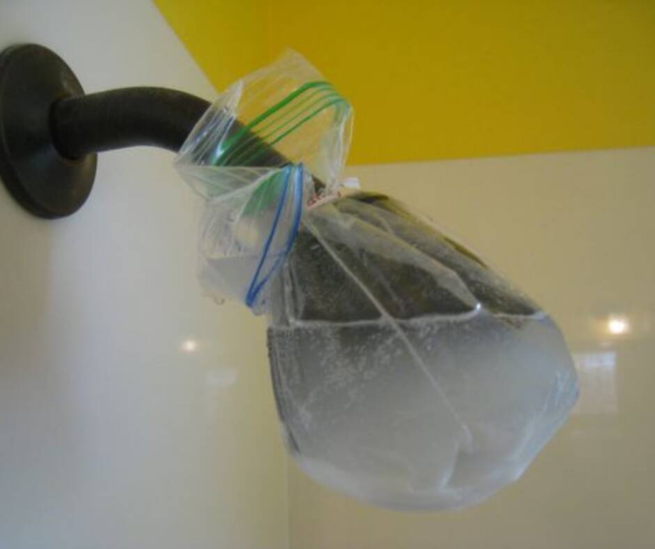 Entfernen von Ablagerungen Schwarzer Duschkopf mit einer Essiggefüllten Tüte umwickelt.