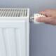 Hand dreht am Thermostatventil eines weißen Heizkörpers – Symbol für Temperaturregelung und Heizungsoptimierung.