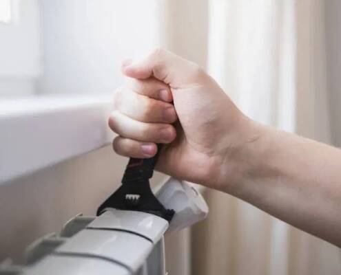 Eine Person verwendet einen Schraubenschlüssel, um ein Heizkörperventil zu öffnen und den Heizkörper zu entlüften.