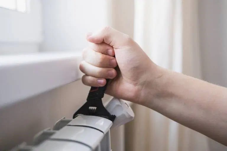 Eine Person verwendet einen Schraubenschlüssel, um ein Heizkörperventil zu öffnen und den Heizkörper zu entlüften.