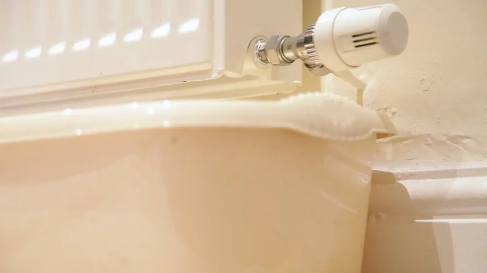 Ein Heizkörper mit angeschlossenem Thermostatventil, darunter ein Auffangbehälter – vorbereitet zur Entwässerung oder Wartung der Heizungsanlage.