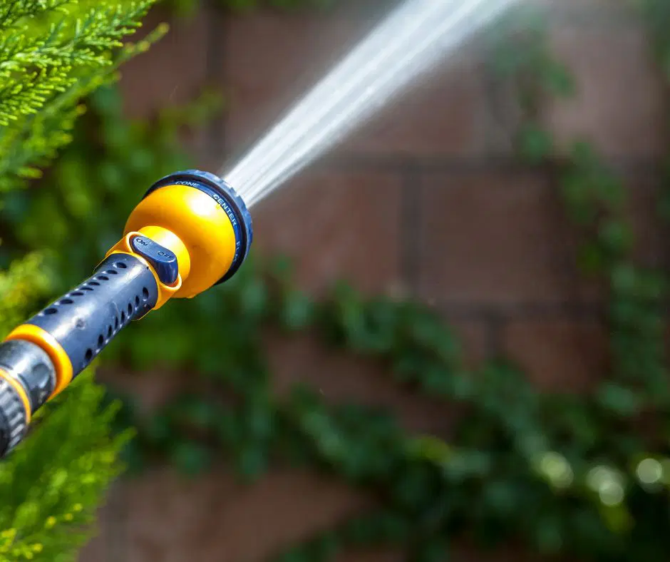 Nahaufnahme eines Gartenschlauchs mit Sprühkopf, aus dem ein kräftiger Wasserstrahl austritt – Verwendung beim Durchspülen eines Heizkörpers im Außenbereich.